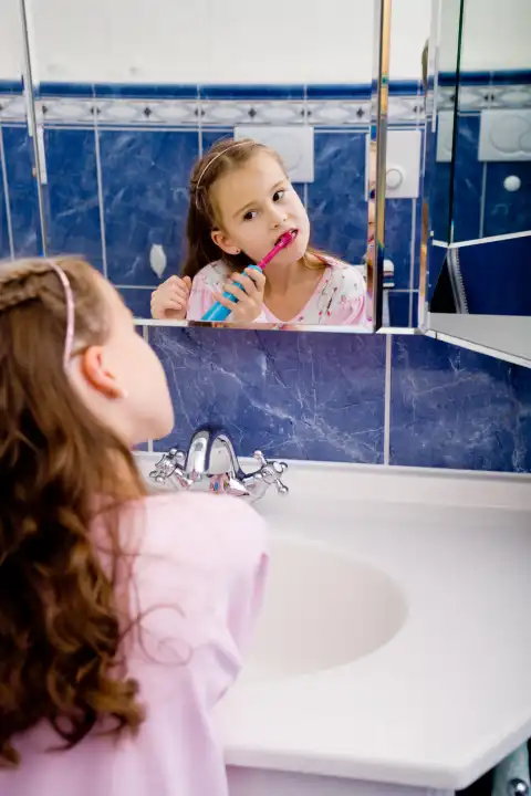 young girl brushing her teeth looking in the mirror