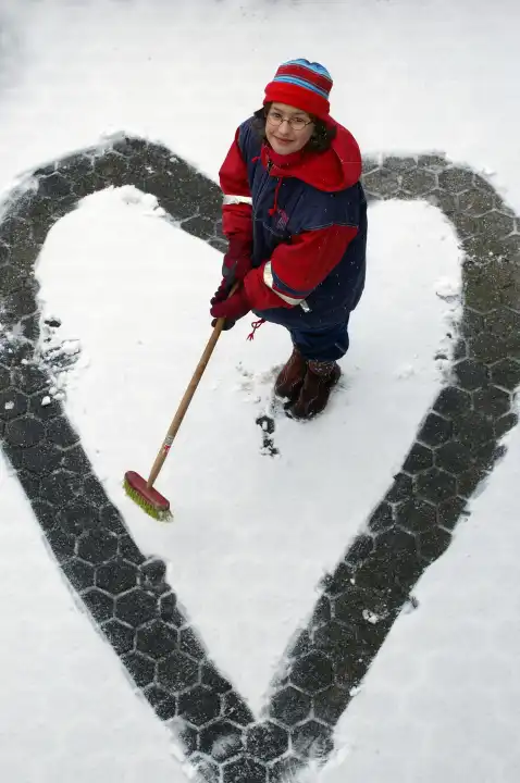 girl with broom paints a heart in the snow
