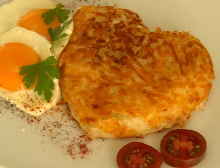Swiss rosti with fried egg and tomato, potato hash brown heart shaped