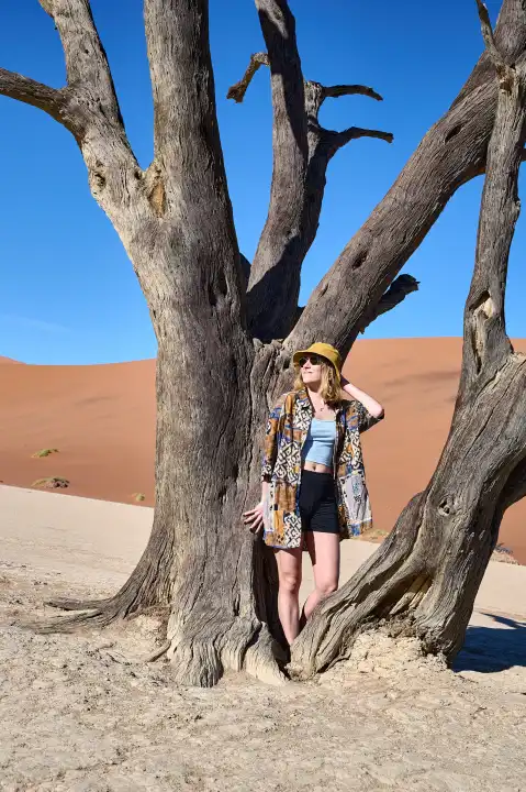 Young woman with sun hat in front of old tree and sand dune