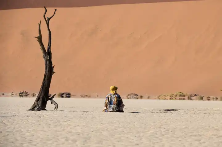 Young woman sitting in front of a dune in Deadvlei
