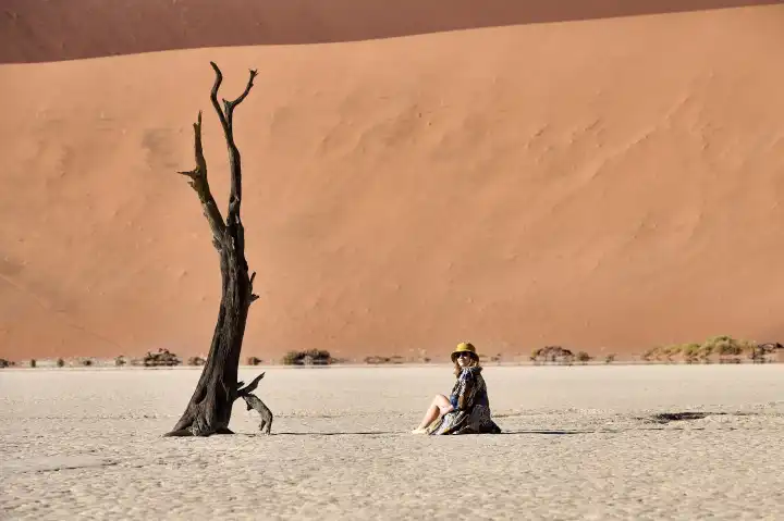 Junge Frau sitzt vor Düne im Deadvlei, Namibia