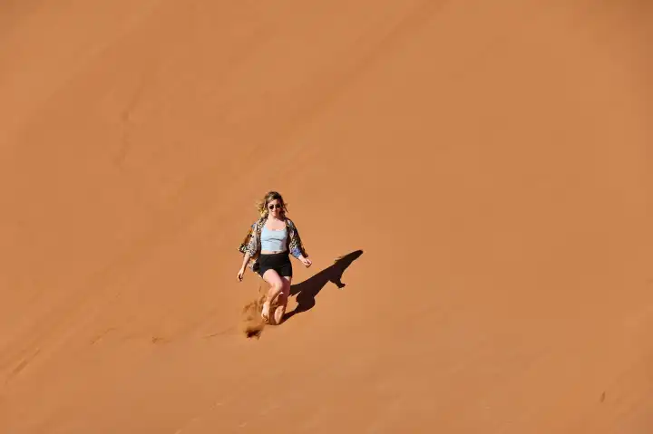 Young woman running down a sand dune