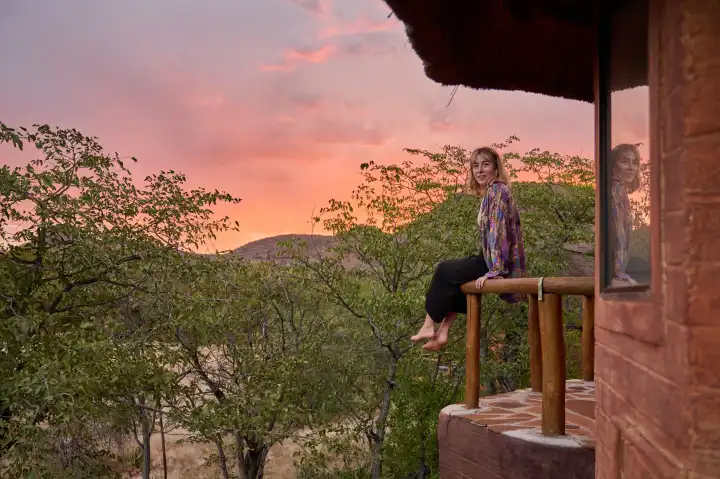 junge Frau sitzt auf einem Balkon vor afrikanischem Abendhimmel
