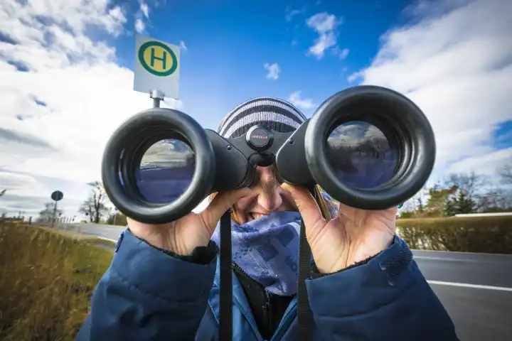 Woman is using binoculars at a bus stop