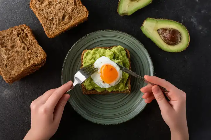 Ansicht von Person Essen Spiegelei und Avocado-Püree auf Toast zum Frühstück, isoliert auf weiss, KI generiert.