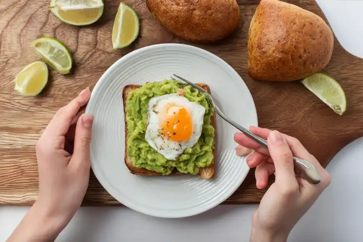 Ansicht von Person Essen Spiegelei und Avocado-Püree auf Toast zum Frühstück, isoliert auf weiss, KI generiert.