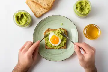 View of person eating fried egg and avocado puree on toast for breakfast, isolated on white, AI generated.