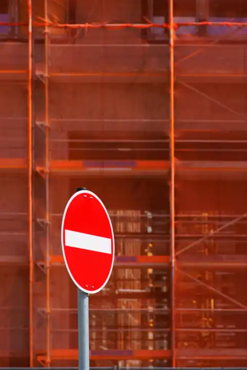 Red one way street sign in front of scaffolding