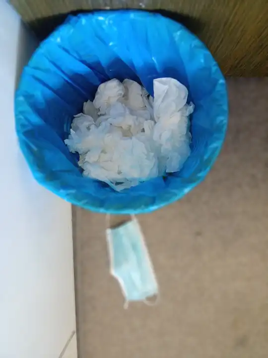 Blaue tasche in einem mülleimer mit servietten und covidmaske auf dem boden