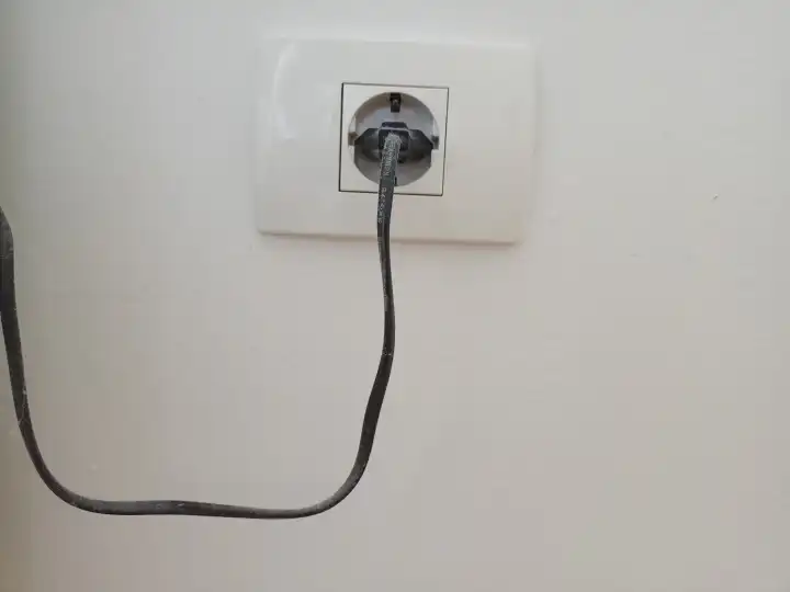 Black cable of some electricity powered machine plugged into wall switch