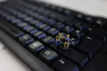 Miniatur-Senioren auf einer Bank an einer Tastatur.