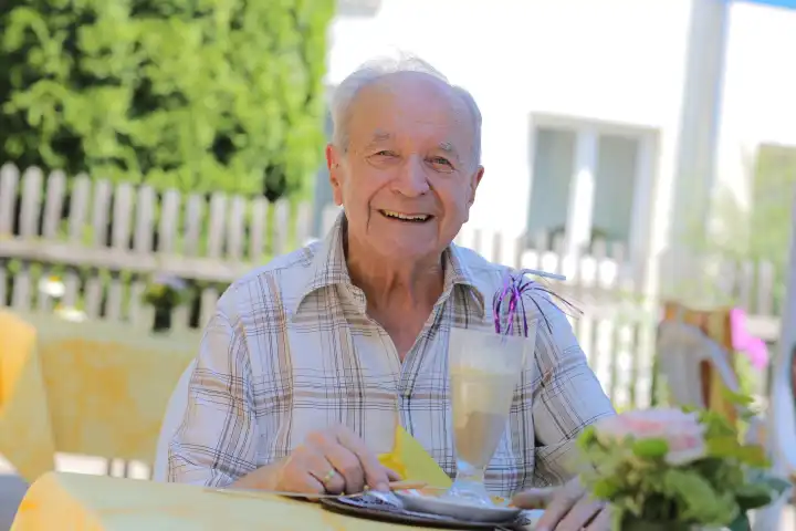 Alter Mann sitzt im Garten mit Getränk