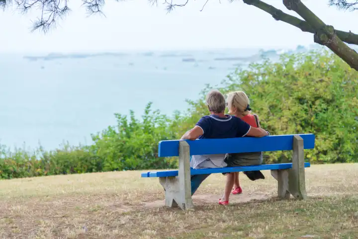 Paar sitzt auf einer blauen Bank und schaut auf das Meer