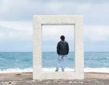 Junger Mann steht in einem Betonquader und schaut auf das Meer
