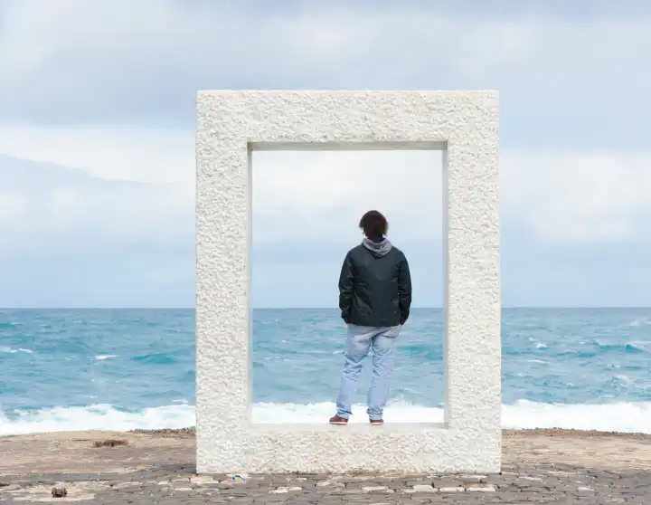 young man standing in a concrete cuboid and looks at the sea