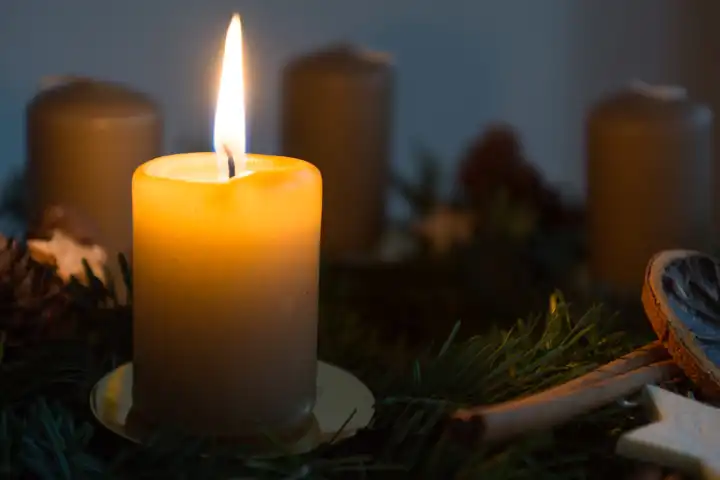 erste Kerze auf dekorativem Adventkranz brennt bei dunkler Umgebung