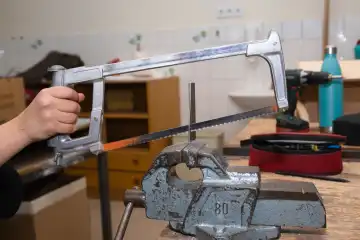 Person saws off with metal saw metal piece on the vice hand, workshop