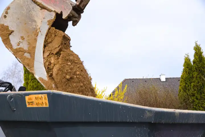 Bucket of a backhoe dumping soil into tipping trough - close-up