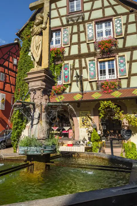 colorful half-timbered house with paintings in the town Kaysersberg, Alsace Wine Route, France, ancient well in front
