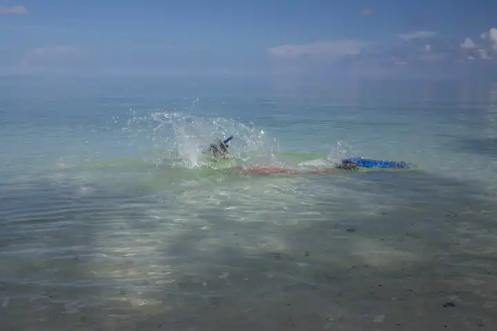 Schnorchlerin in farbigem Tauchanzug spritzt im seichten Wasser der Bandasee
