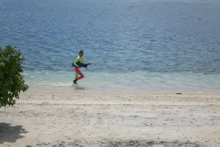 female snorkeler in colorful divesuit running through shallow water on a sandy beach