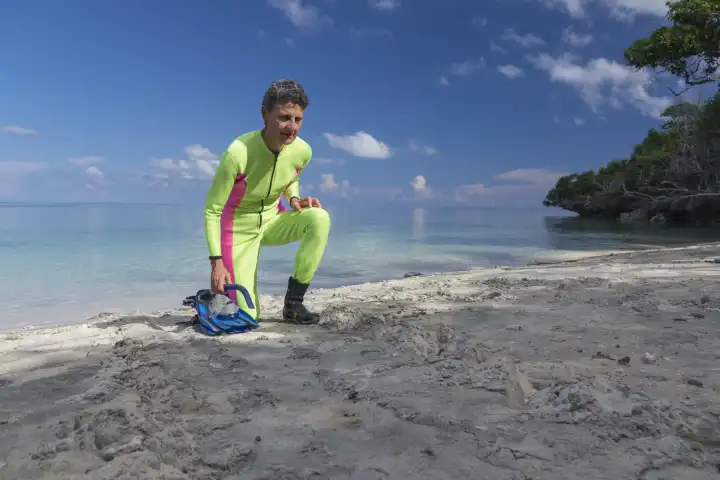 female snorkeler in yellow divesuit discovers turtle tracks on the beach. in the back sea, blue sky, white clouds.