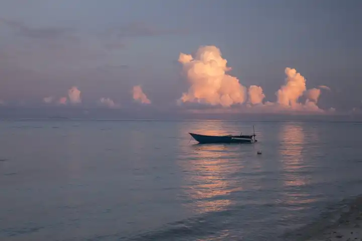 Indonesian outrigger canoe on the sea in gentle evening light, rosy cumulus clouds in the background