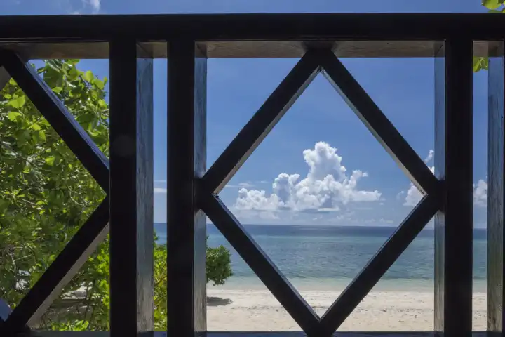 view through wooden balustrade on sandy coral beach, sea, blue sky and white cumulus