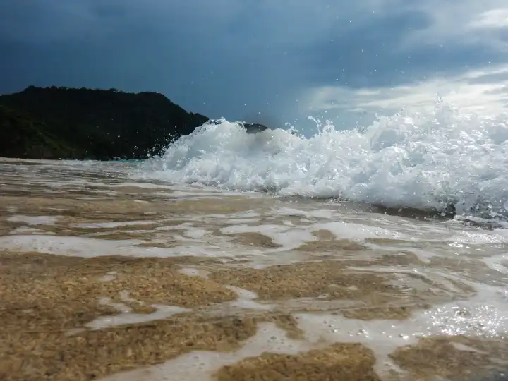 Gewitterstimmung, Welle bricht sich am Strand, über Sandstrand ablaufendes Wasser im Vordergrund