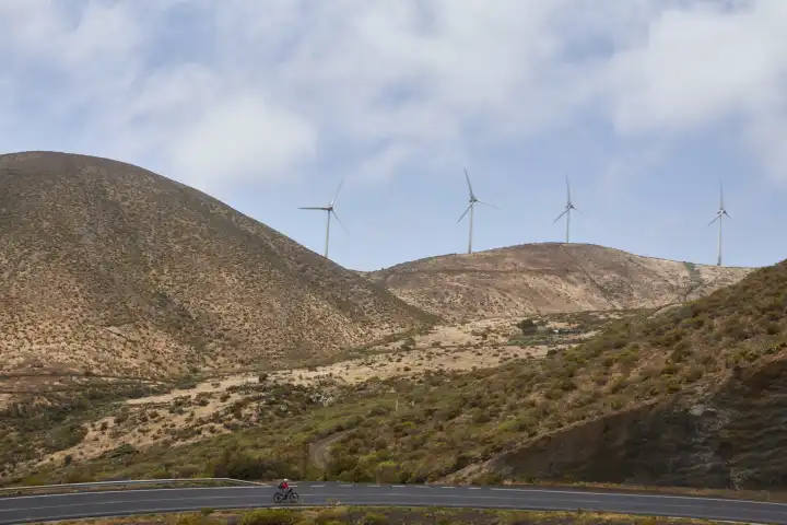 Vier Windturbinen auf kargem Hügel, im Vordergrund Radfahrer auf Strasse. El Hierro, Kanarische Inseln, Spanien