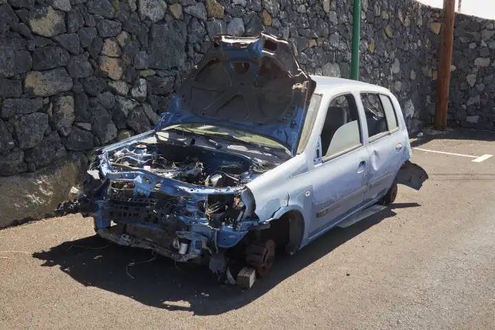 Light blue junk car dumped in public parking lot in front of dry stone wall. El Hierro, Canary Islands, Spain