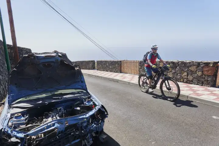 Mountainbikerin fährt an hellblauem schrottauto auf öffentlichem Parkplatz vorbei. El Hierro, Kanarische Inseln, Spanien