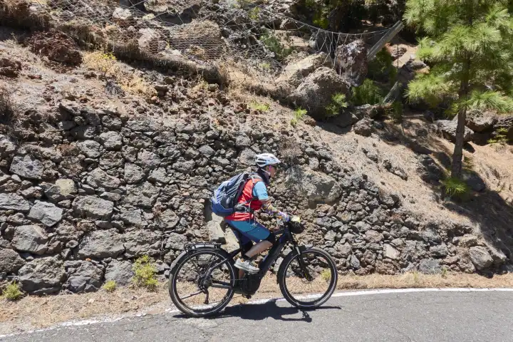 Mountain biker rides past rockfall protection device on mountain road. El Hierro, Canary Islands, Spain