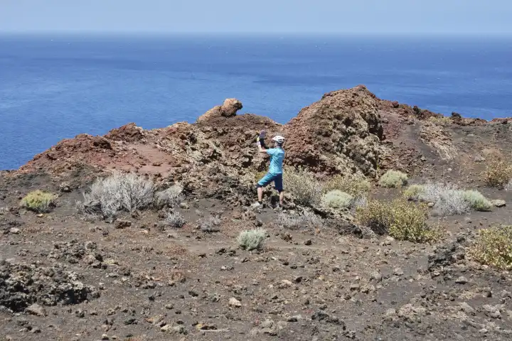 Sportliche Frau in türkis fotografiert mit Tablet Lavagestein mit blauem Meer im Hintergrund. El Hierro, Kanarische Inseln, Spanien