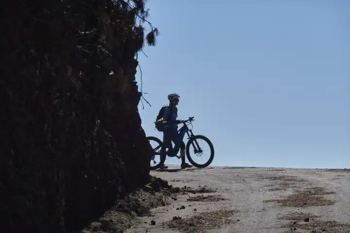 mountainbikerin schaut ins Blaue. Im Vordergrund dunkle Mauer. La Palma, Kanarische Inseln
