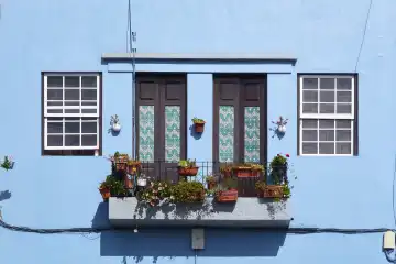Partial view of a light blue house façade with green balcony and 2 windows. La Palma, Canary Islands, Spain