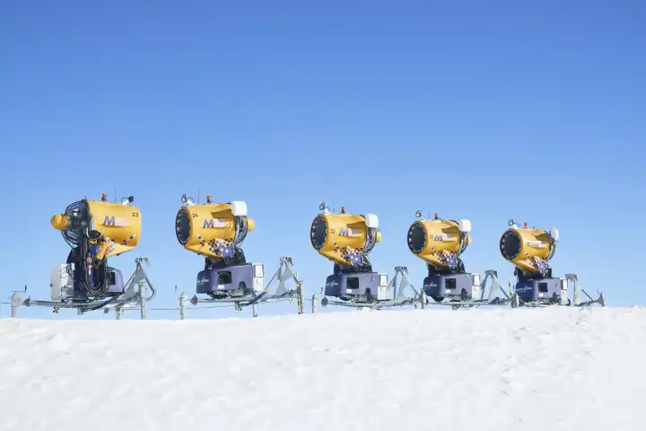 5 gelbe Schneekanonen auf schnee, freigestellt gegen den blauen Himmel. Wallis, Schweiz
