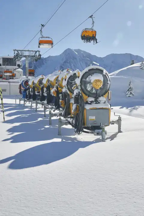 Mehrere Schneekanonen hintereinander aufgereiht mit Sesselbahn und Bergpanorama.
Wallis, Schweiz
