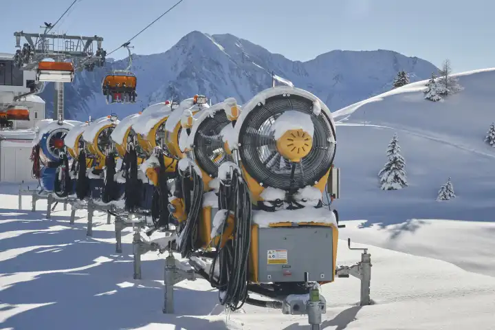 Mehrere Schneekanonen hintereinander aufgereiht mit Sesselbahn und Bergpanorama.
Wallis, Schweiz