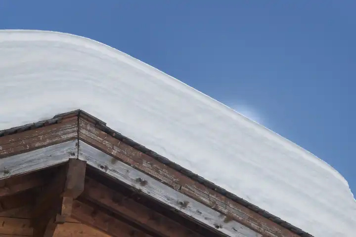 Roof gable with half a meter of snow. Finely glittering edge due to backlighting. Valais Switzerland