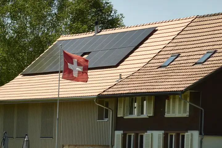 Converted, renovated farmhouse with solar panels and waving Swiss flag. Zurich Oberland, Switzerland.