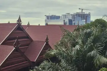Satteldächer mit verzierten Giebeln und Palmen, im Hintergrund modernes Hochhaus im Bau. Makassar, Sulawesi, Indonesien