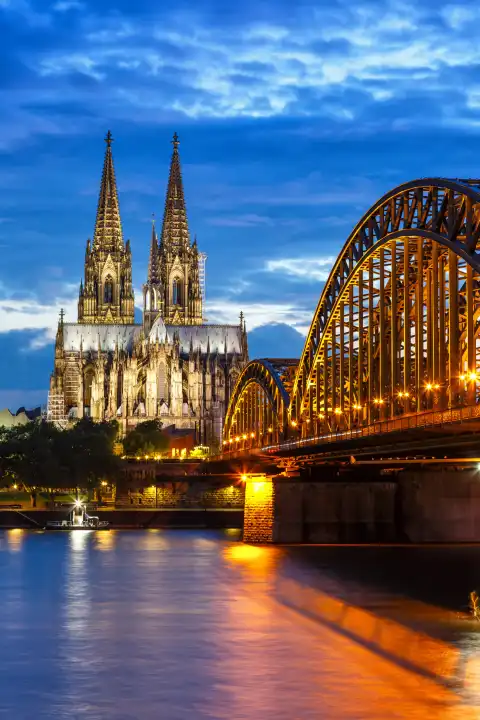 Cologne, Germany - August 3, 2021: Cologne Cathedral skyline and Hohenzollern Bridge with river Rhine in Germany at night vertical format in Cologne, Germany.