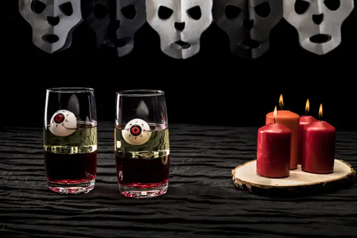 2 Gläser mit Augäpfeln auf einem Tisch mit Kerzen und Totenkopfgirlande, Helloween, Studioaufnahme