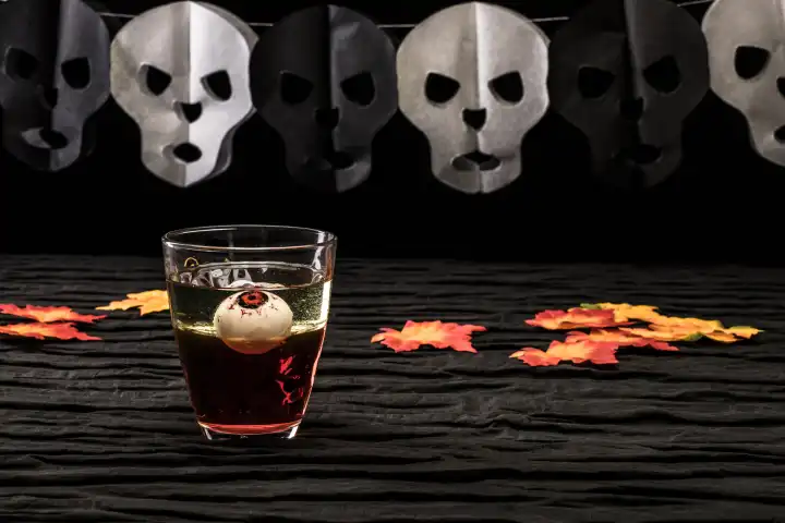 Getränk mit einem Augapfel,Halloween, auf dunklem Untergrund und Totenköpfen im Hintergrund,Studioaufnahme