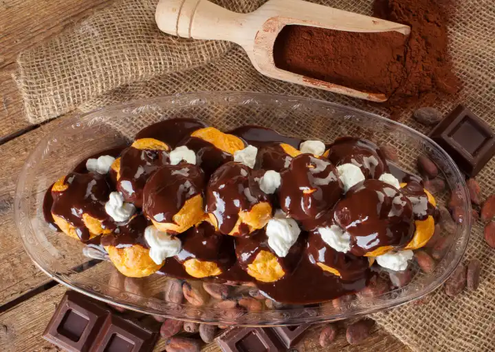 Chocolate profitteroles with cream, cocoa powder, cocoa beans and pieces of chocolate