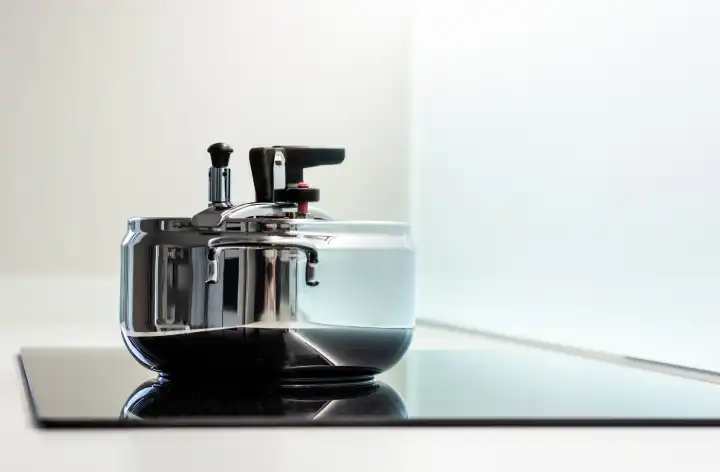 Stainless steel pressure cooker on a modern induction cooking hob.