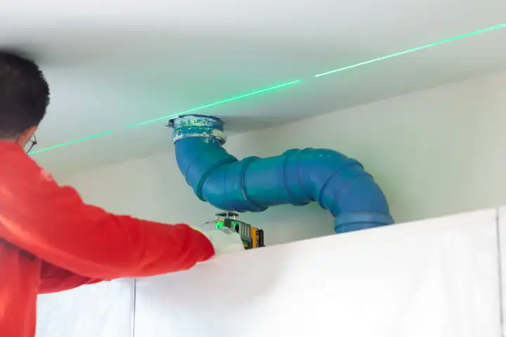 A plasterer takes measurements with a laser level to create a wall above the kitchen cabinets.