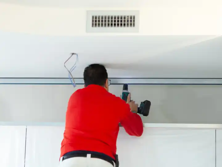Plasterboard worker installs a plasterboard wall on the kitchen cabinets to cover the extractor pipe of the hood.